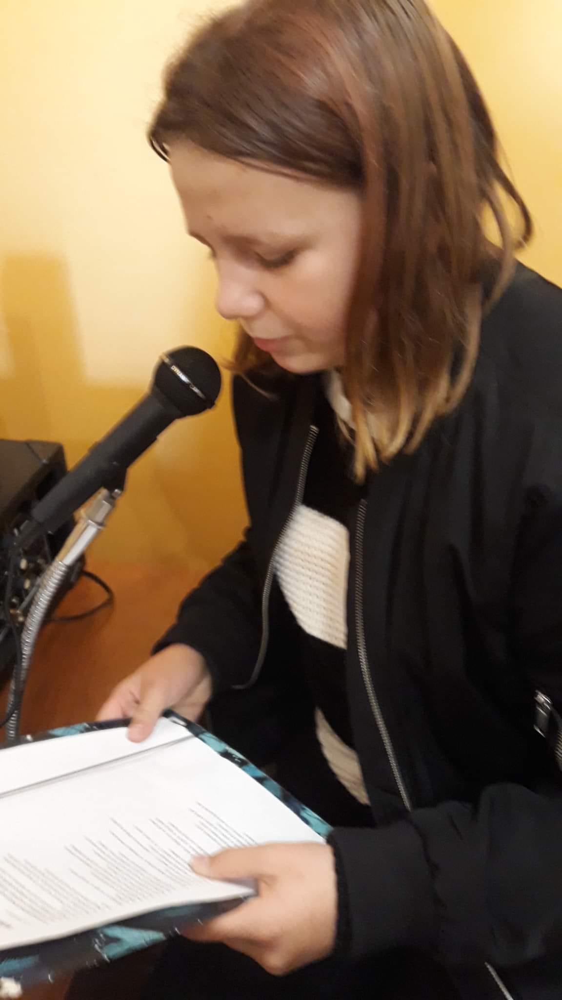 Uczennica przy mikrofonie czyta tekst utworu