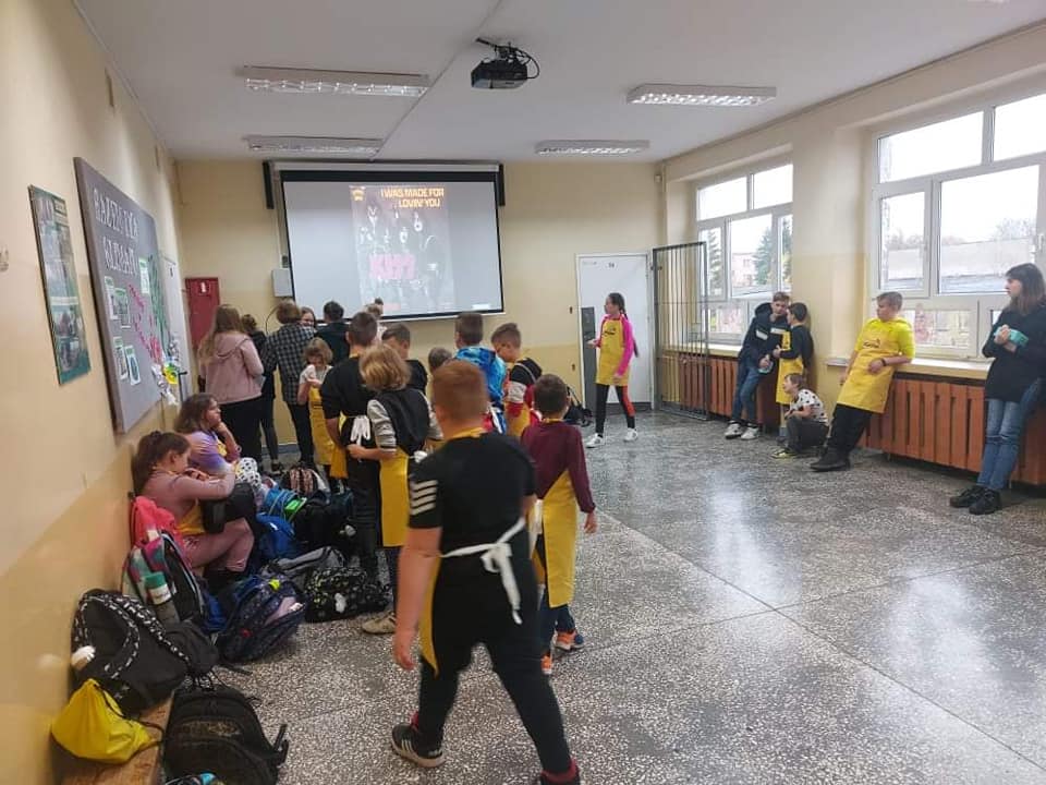 uczniowie na korytarzu w czasie przerwy, w tle ekran  i wyświetlany tekst piosenki