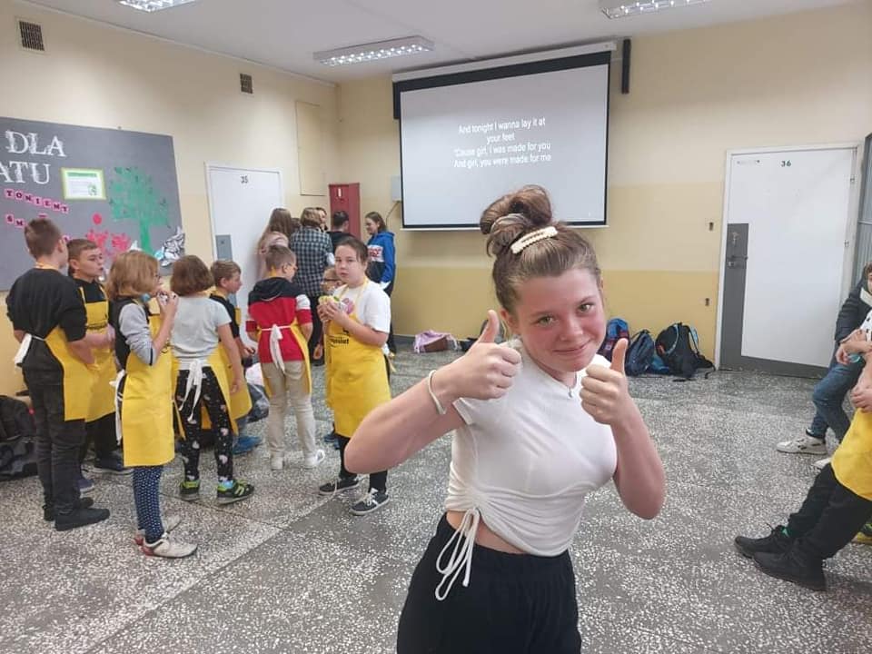 uczniowie na korytarzu w czasie przerwy, w tle ekran  i wyświetlany tekst piosenki